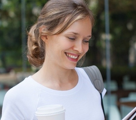 Image of woman smiling while outside and holding a coffee