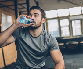 man in weight room drinking water after working out