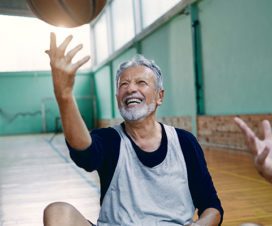 man throwing a basketball up as he sits with friends in a gym