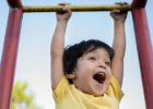 Child playing on monkey bars while caregivers discuss pediatric spine care.