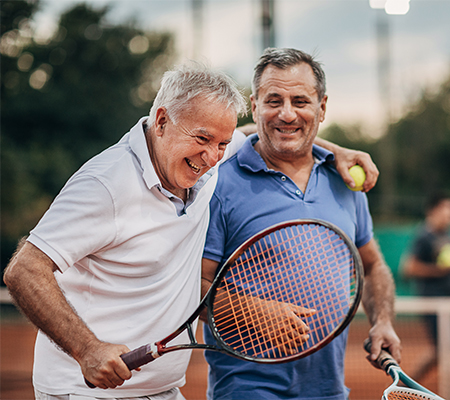 Two older men displaying how an implanted Baclofen pump doesn't need to limit daily activities like playing tennis or socializing with friends. 