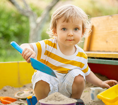 A young boy shoveling sand in a sandbox
