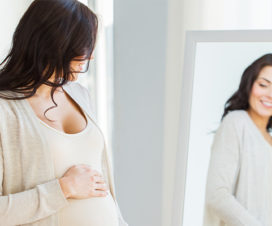 A pregnant women holding her belly and looking in the mirror with a smile.