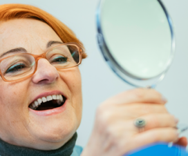 Woman looking at her dental implants in a mirror.
