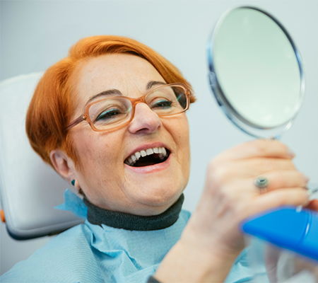 Woman looking at her new dental implants in a mirror.