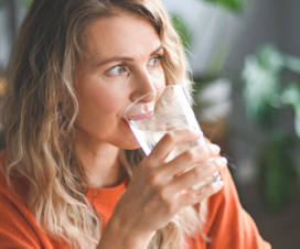 Young woman with orange shirt drinking glass of water.