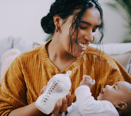 A woman bottle feeding her baby wondering if she should be breastfeeding versus pumping