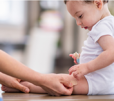 Infant getting band-aid placed on their leg by an adult after adhering to the childhood immunization schedule