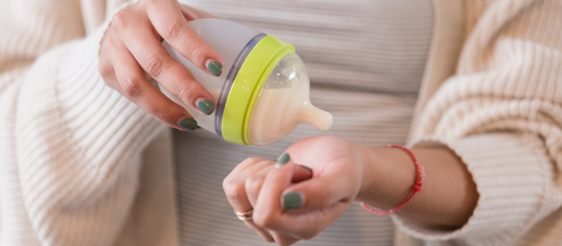 A woman checking the temperature of a bottle of milk on her wrist.
