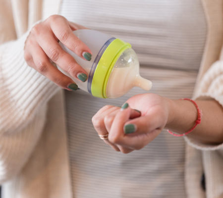 A woman checking the temperature of a bottle of milk on her wrist.