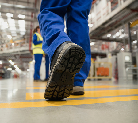 A person walking showing the bottom of their workplace safety shoes in a warehouse. 