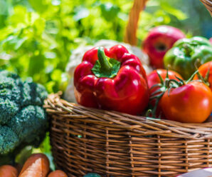 Photo of bell peppers and tomatoes in a basket surrounded by other fresh produce
